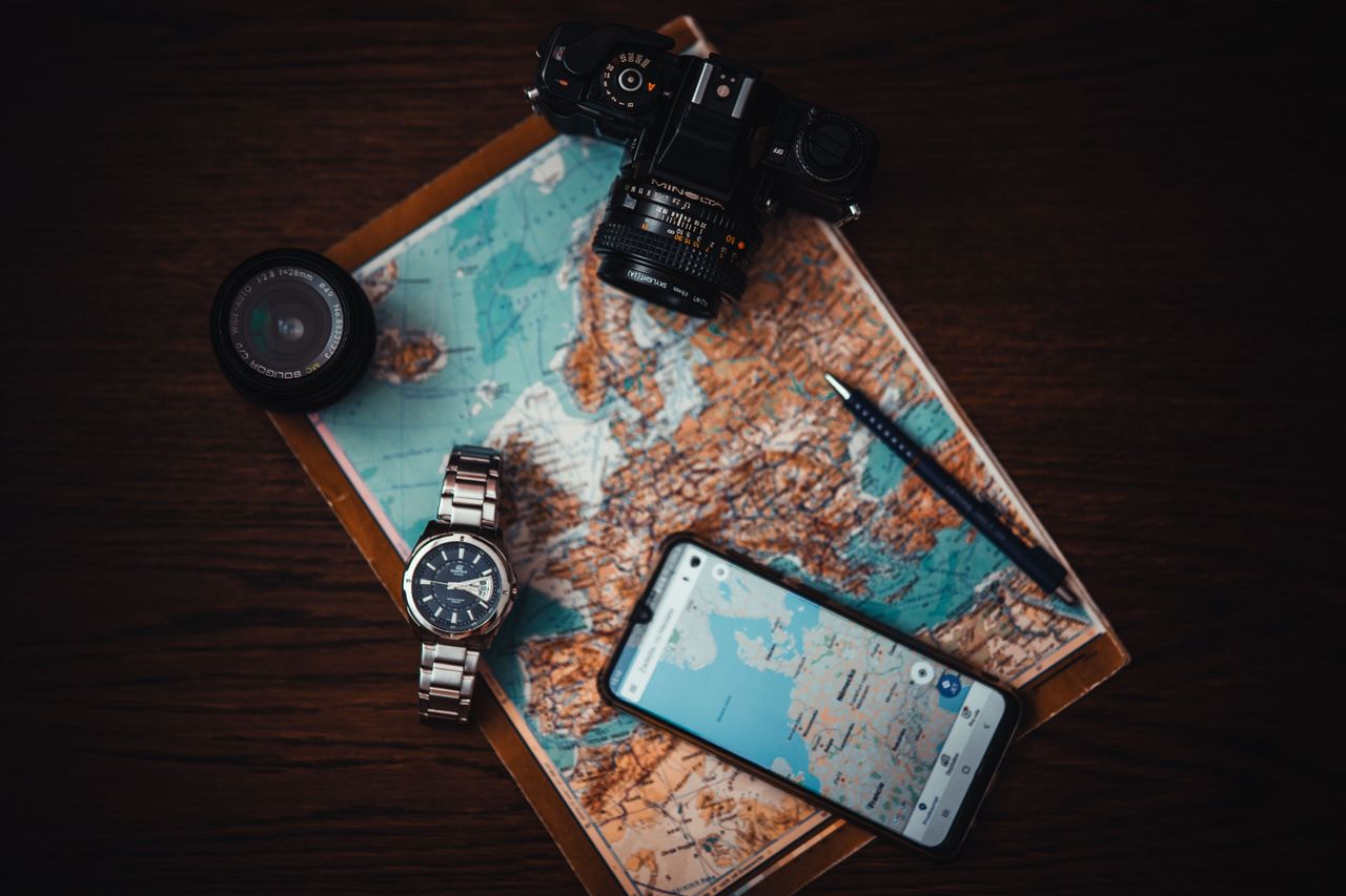 services-01 Top view of travel essentials including a map, camera, phone, watch, and lens on a wooden surface.