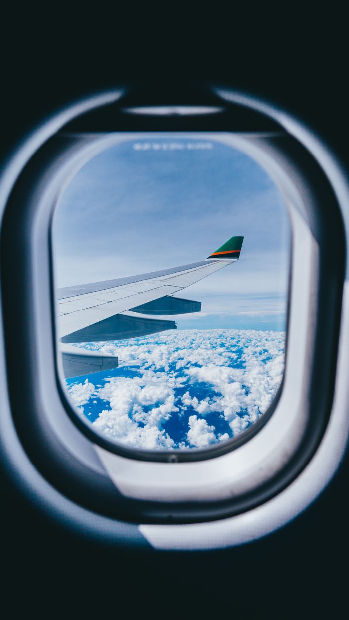 Scenic view of aircraft wing and sky seen through a plane window, captured in flight.